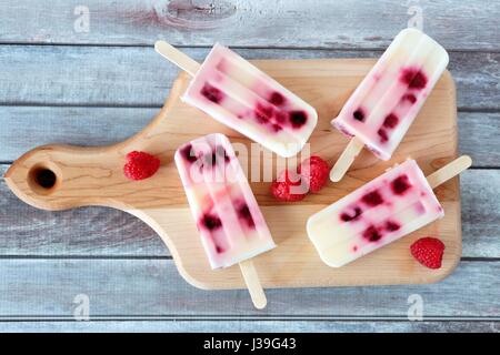 Homemade raspberry vanilla popsicles on a paddle board with rustic wood background Stock Photo