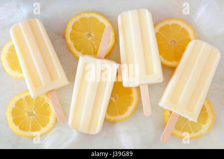 Healthy lemon yogurt popsicles with fresh lemon slices scattered on a white marble background Stock Photo