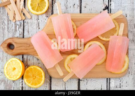 Pink lemonade popsicles with lemon slices on a paddle board with rustic wood background Stock Photo