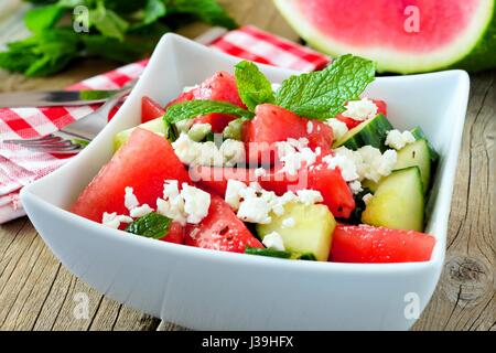 Delicious watermelon, cucumber and feta cheese salad in square bowl on wood background Stock Photo
