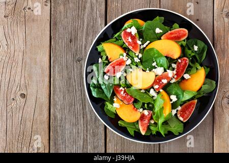 Autumn salad of arugula, spinach figs and goat cheese in a black plate, above view on a rustic wooden background Stock Photo