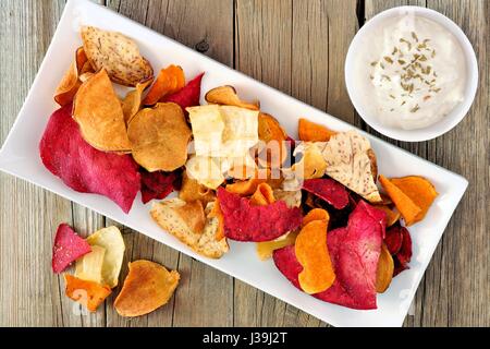 Plate of colorful organic vegetable chips with dip downward view on rustic wood Stock Photo