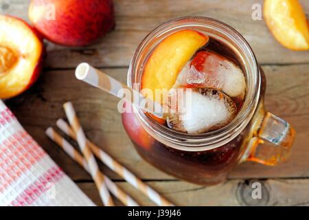 Mason jar glass of homemade peach iced tea on a rustic wooden background, downward view Stock Photo