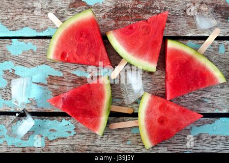 Group of watermelon slice popsicles on a rustic blue wood background Stock Photo