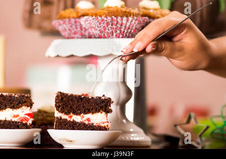 Delicious chocolate cake pieces with cream filling sitting on small plates, hand holding fork grabbing piece, pastry concept Stock Photo