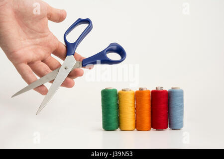 Multicolor Sewing Threads, Bobbins With A Hand Holding A Scissor Isolated on White Background. Stock Photo