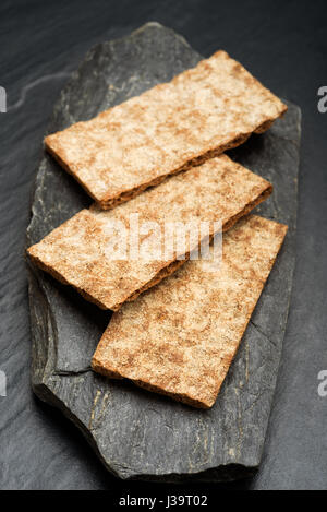 Three tasty rye crisp bread slices without topping on black stone. Crisp bread is part of the traditional Nordic culinary culture. Stock Photo