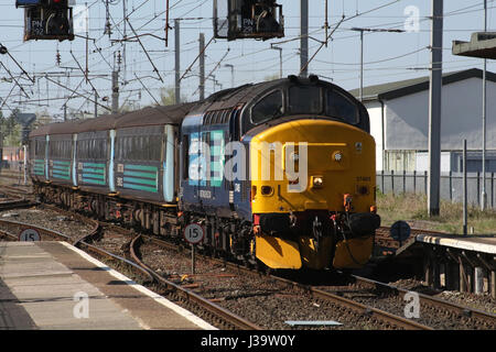 Class 37 diesel electric locomotive 37405 in DRS livery with loco hauled passenger train for Northern arriving at Carnforth railway station. Stock Photo