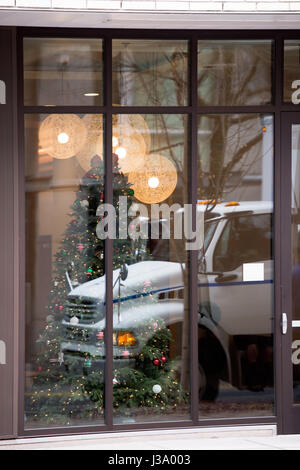 Reflection of white semi truck cab in a large windows of urban building with a glass wall behind which the foredeck room with decorated Christmas tree Stock Photo