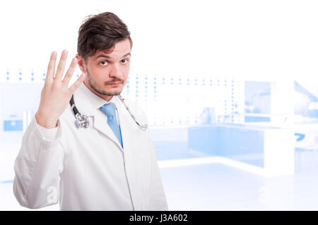 Male medic in medical uniform and stethoscope holding hand up with four fingers and copyspace Stock Photo