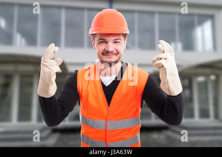 Cheerful architect with fingers crossed from both hands feeling lucky in front of building Stock Photo