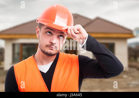 Portrait of handsome constructor holding his hardhat on head in front of house Stock Photo
