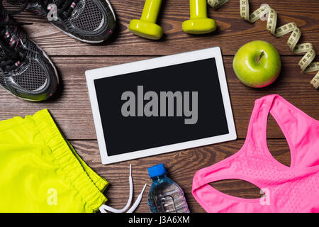White digital tablet with female fitness accessories on wooden background