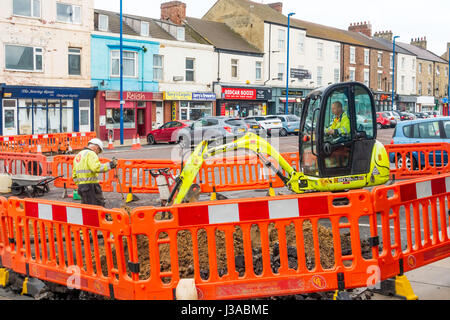 Workman using a small 8018CTS JCB mini excavator trenching for a power cable replacement a road in a town centre site Stock Photo