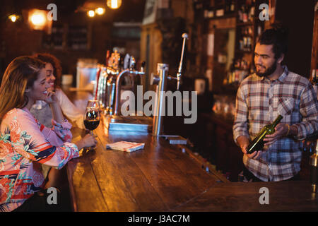 Bartender showing wine bottle to women at counter in pub Stock Photo