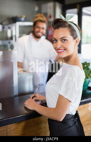 Smiling waitress writing on notepad with chef in background Stock Photo