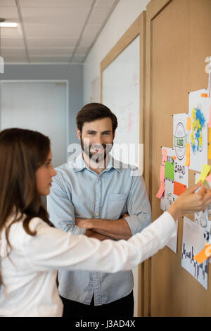 Smiling businessman with female colleague analyzing charts on soft board at office Stock Photo