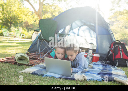 Siblings using laptop outside the tent at campsite Stock Photo
