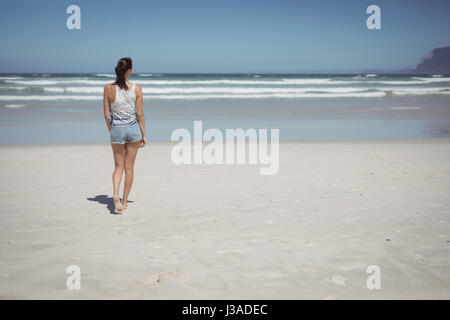 Rear view of woman walking at beach during sunny day Stock Photo