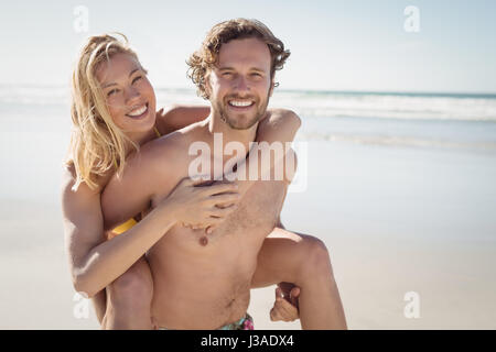 Portrait of young man piggybacking beautiful woman at beach during sunny day Stock Photo