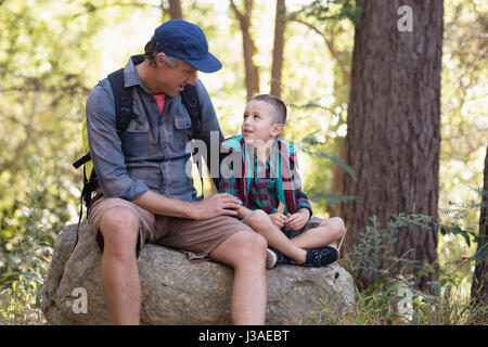 Father and son discussing while sitting on rock Stock Photo