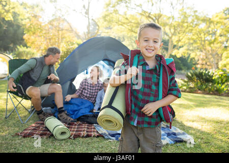 Portrait of boy holding a rolled mat while family sitting in the tent Stock Photo
