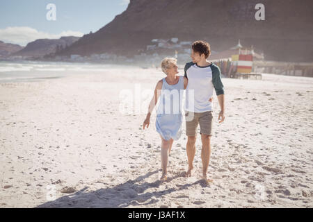Young man with his mother walking on sand at beach during sunny day Stock Photo