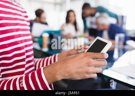 Midsection of businesswoman using phone while sitting with colleagues at desk in office Stock Photo