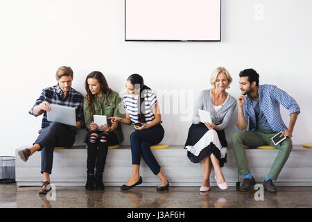 Business people using technologies while sitting against wall in office Stock Photo