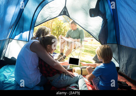 Kids and mother using tablet while father looking at the map at campsite Stock Photo
