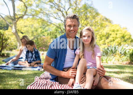 Portrait of smiling daughter sitting on fathers lap in park on a sunny day Stock Photo