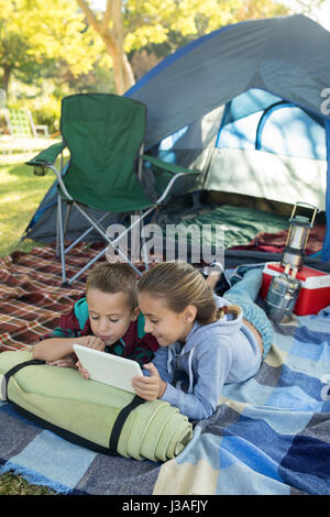 Siblings using laptop outside the tent at campsite Stock Photo
