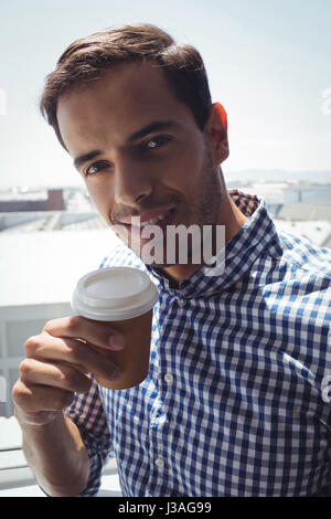 Close up portrait of thoughtful young businessman holding coffee cup by window in office Stock Photo