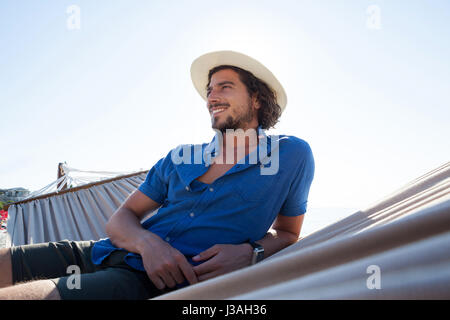 Smiling looking away while relaxing on hammock at beach during sunny day Stock Photo