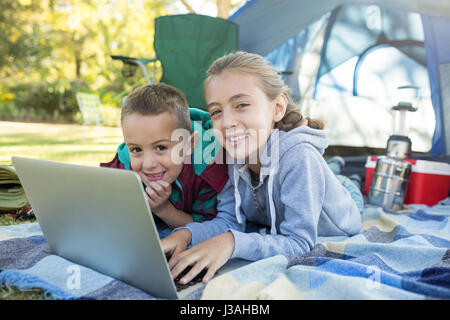 Smiling siblings using laptop outside the tent at campsite Stock Photo