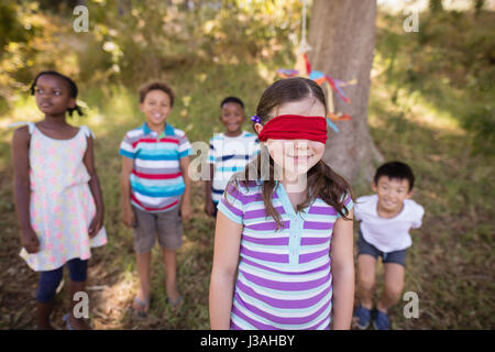 Friends looking at blindfolded girl standing on grassy field in forest Stock Photo