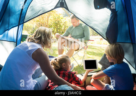 Kids and mother using tablet while father looking at the map at campsite Stock Photo
