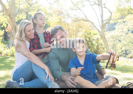 Family looking at boy playing with toy airplane in park Stock Photo