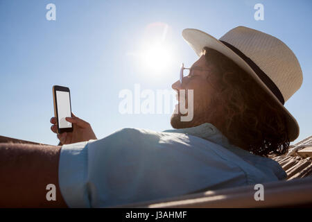 Smiling man relaxing on hammock and using mobile phone on the beach Stock Photo
