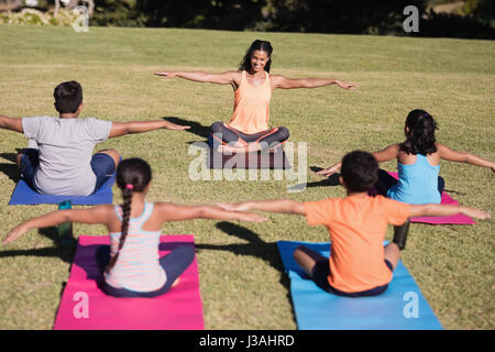 Happy young female trainer teaching stretching exercise to children at park Stock Photo