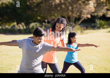 Young female trainer examining children praciticing Virabhadrasana II pose on mat Stock Photo