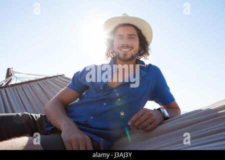 Portrait of smiling man relaxing on hammock at beach during sunny day Stock Photo