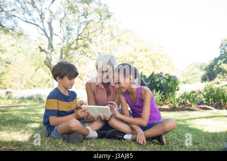Grandmother and grand kids using digital tablet in the park on sunny day Stock Photo