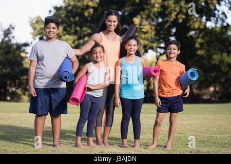 Portrait of children and female instructor holding exercise mat at park Stock Photo