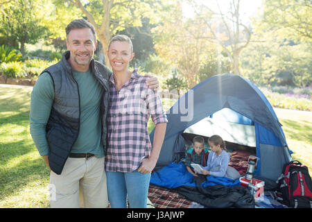 Couple smiling at camera while kids sitting in tent at campsite Stock Photo