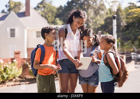 Happy teacher and children using digital tablet on street during sunny summer trip Stock Photo