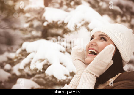 Young beautiful woman in winter park, touching her face skin,  laughing and looking up. Selective focus, copy space, vintage toned image Stock Photo