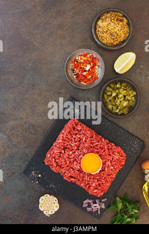 Beef tartare with an egg yolk and other ingredients on rustic textured background  Top view, blank space Stock Photo
