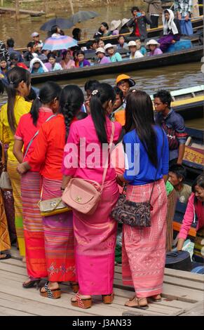 A line of young Burmese girls dressed in elegant, traditional brightly-coloured clothes queue for a boat at Phaung Daw Oo Festival, Inle Lake, Myanmar Stock Photo