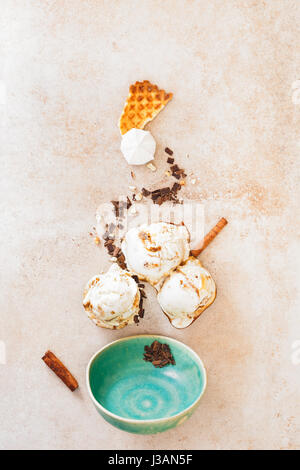 Ice cream with melting scoops, various ingredients and empty vintage bowl on rustic surface, flat lay Stock Photo